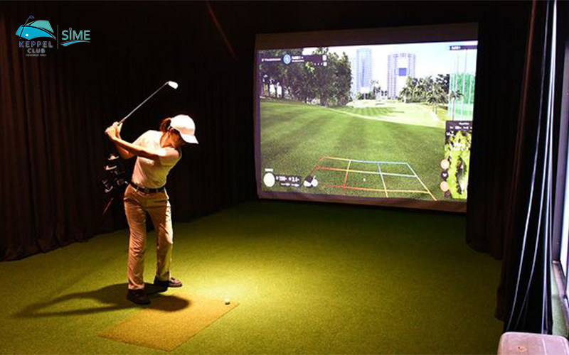 woman playing golf indoors at Keppel Club’s golf simulation room with a projected golf course background